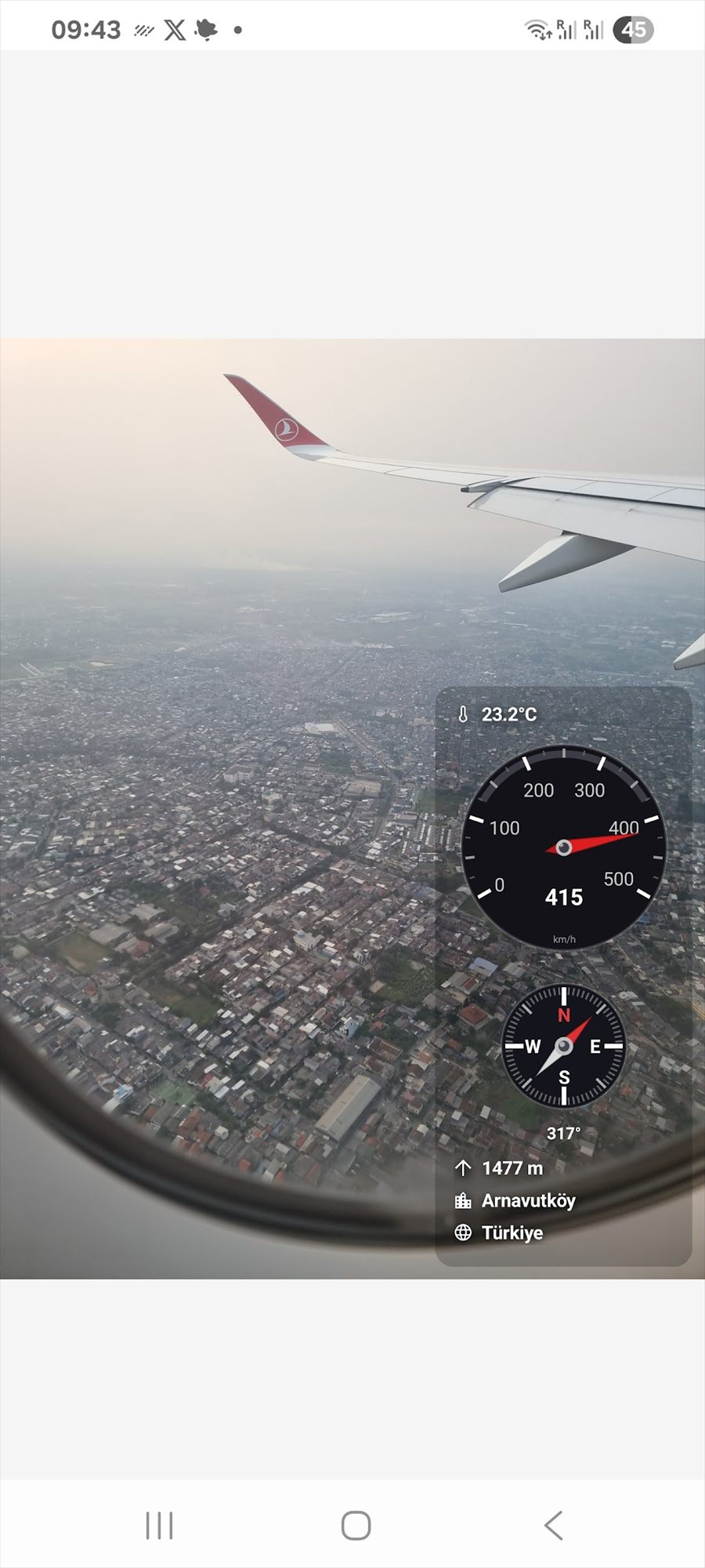 MemoCam viewfinder over a city from a plane window, showing a speedometer at 415 km/h, 23.2 °C, a compass at 317°, 1477 m altitude and the city name.