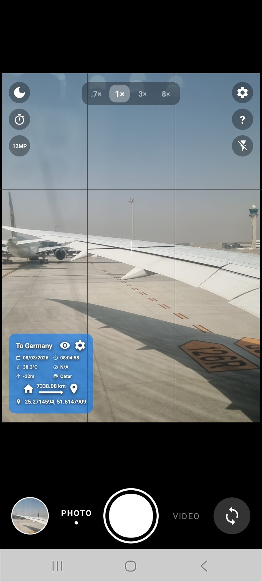 An aeroplane wing on an airport apron, with an overlay reading To Germany, 38.3 degrees Celsius, Qatar, and 7338.08 km from home.