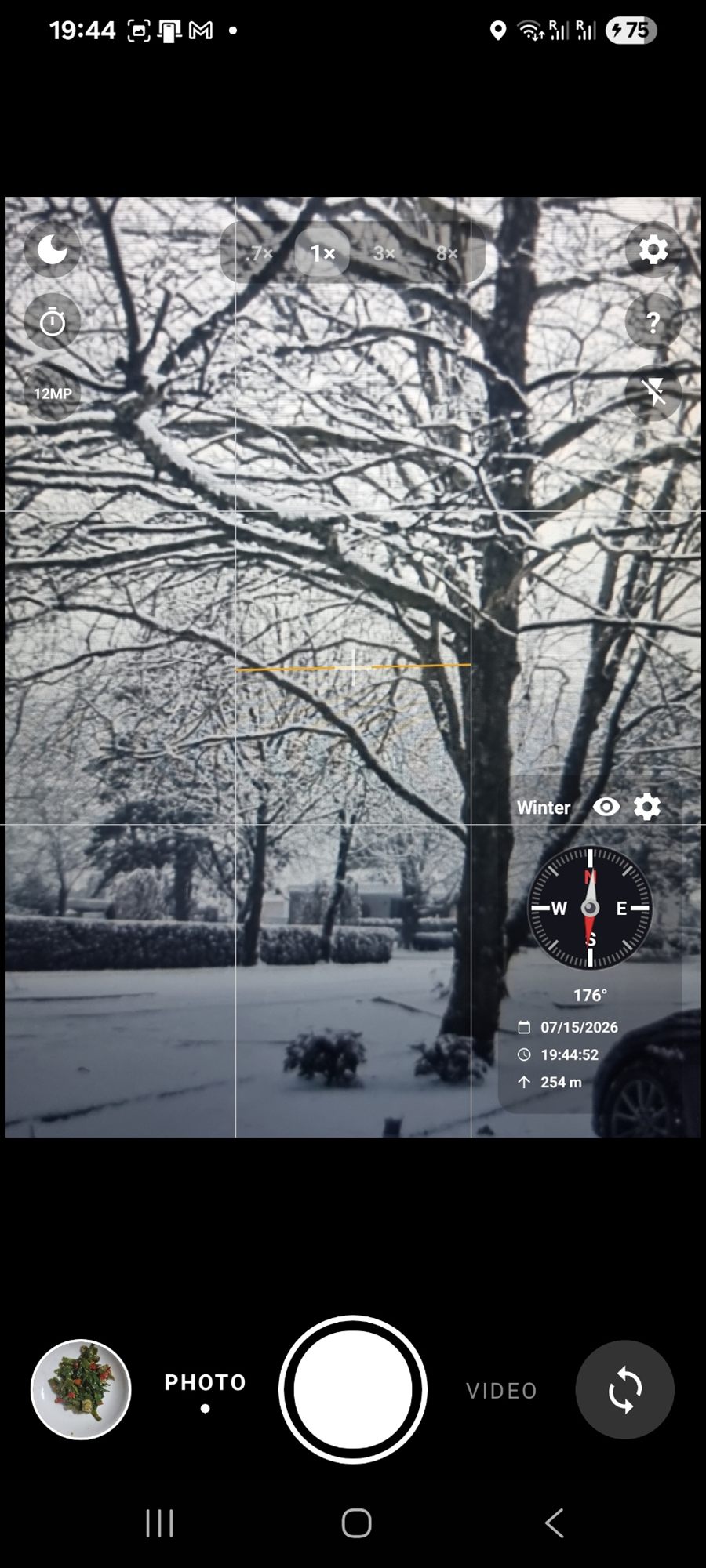 Snow-covered trees in a garden, with a compass at 176 degrees, the date, the time and 254 m altitude.